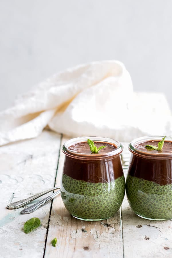 two small jars of mint chia pudding with chocolate on top and a white napkin in the background