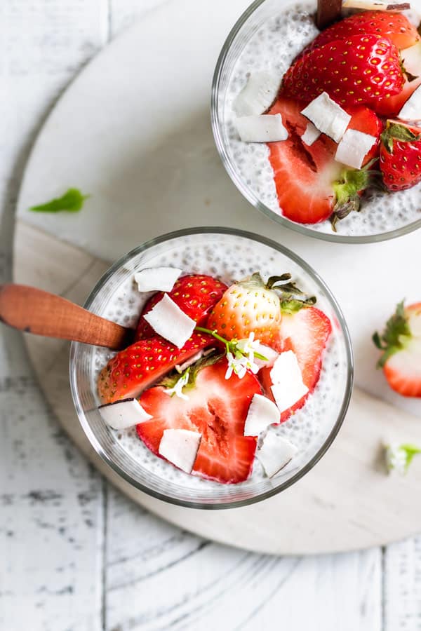 a top down view of two cups of chia pudding with strawberris and flaked coconut on top