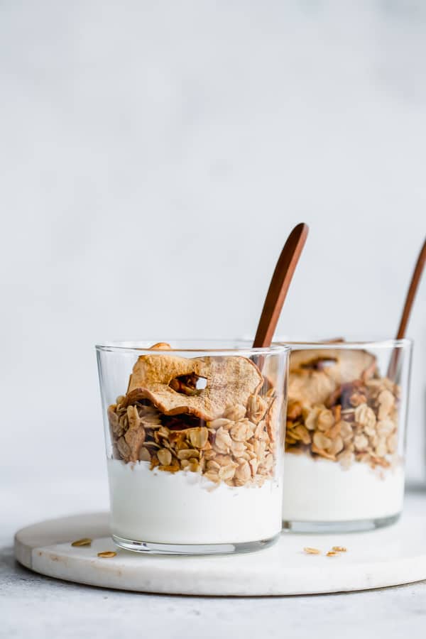 Two glasses of yogurt parfaits with apple granola in them