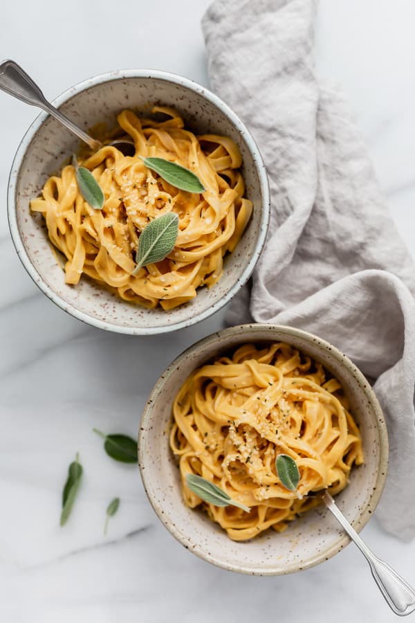 Two bowls of vegan pumpkin pasta with a grey napkin on the side