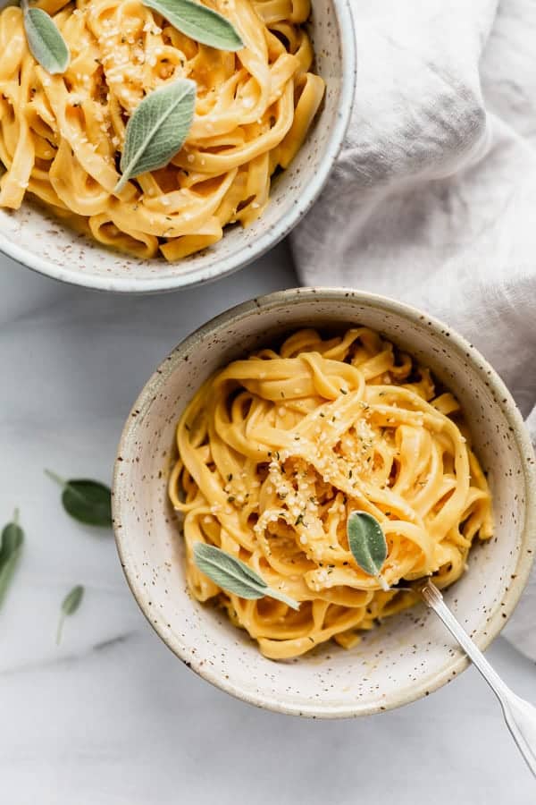 Two bowls of linguine pasta in a pumpkin alfredo sauce topped with fresh sage leaves