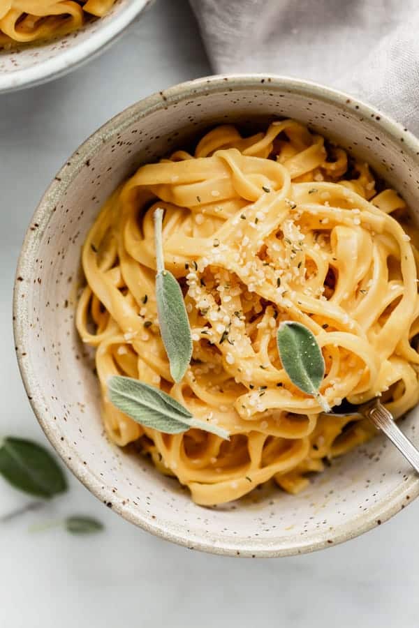 A bowl of pasta with pumpkin Alfredo sauce and sage on top