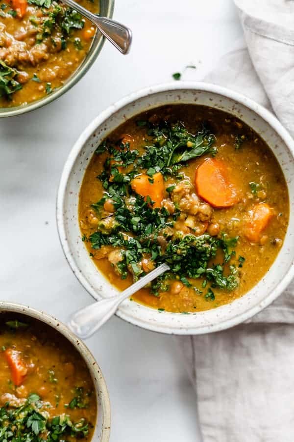 a bowl of slow cooker lentil soup topped with chopped parsley and carrots 