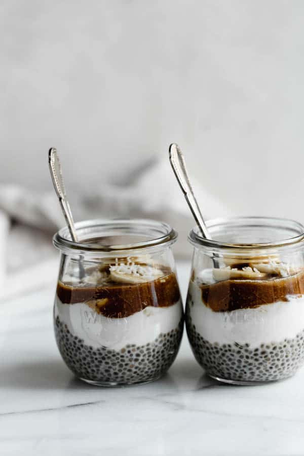 small jars filled with chia pudding, bananas, and a caramel sauce