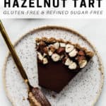 A vegan chocolate hazelnut tart topped with crushed hazelnuts on a plate