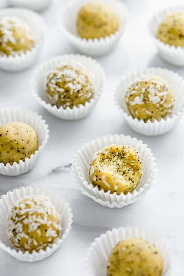 energy bites on a marble board covered in coconut shreds and in white baking cups