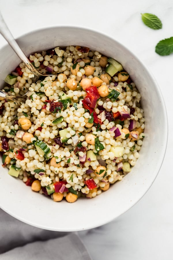 Israeli couscous salad in a large bowl with serving spoons