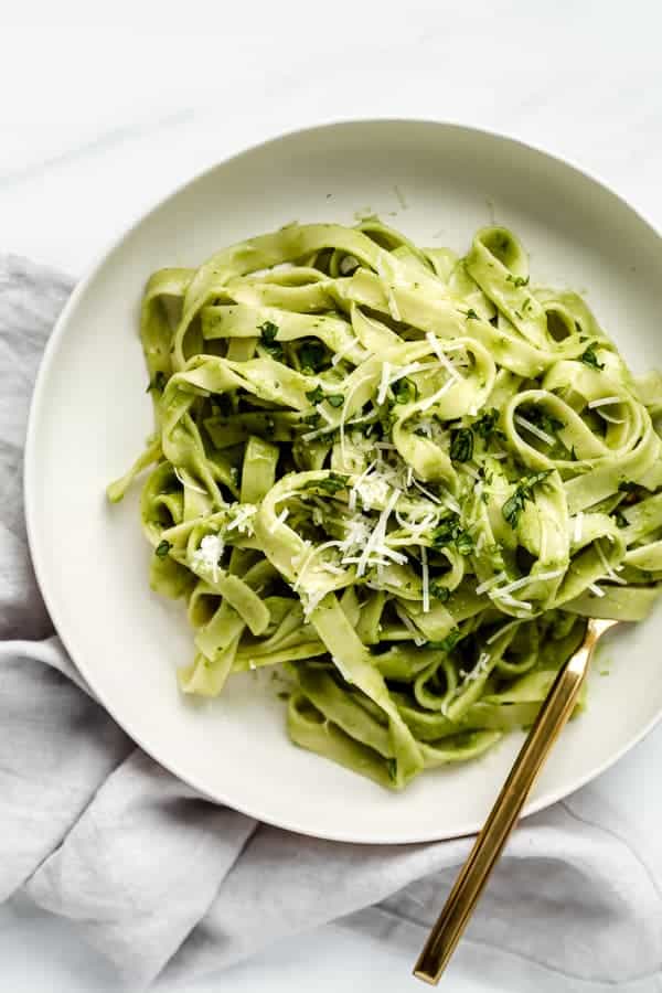 a white plate with avocado pasta on it   