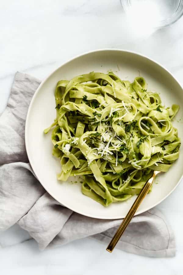 a plate of avocado pasta with a napkin and glass of water 