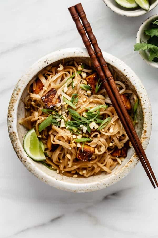 a bowl of vegan pad thai in a bowl on a white marble board