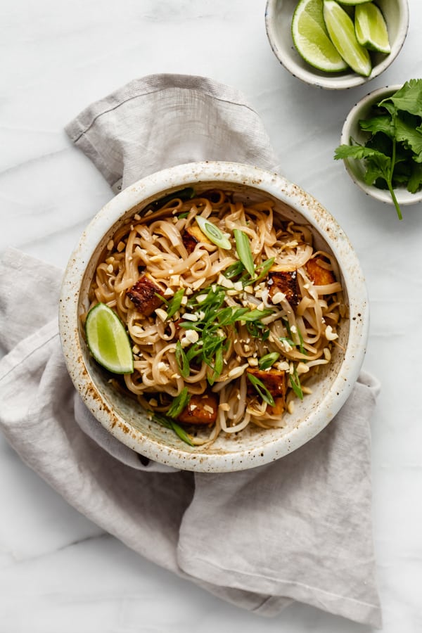 a bowl of vegan pad thai on a grey napkin with a side of cilantro