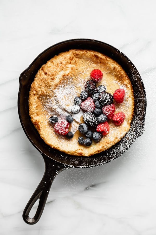 Dutch baby pancake in a cast iron skillet topped with berries and powdered sugar 