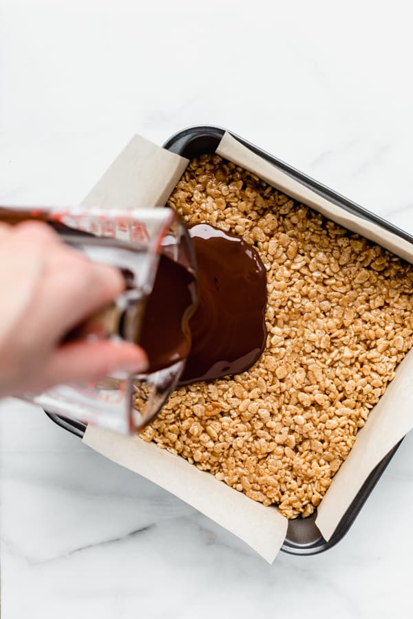 a hand pouring chocolate on a pan of scotcheroos