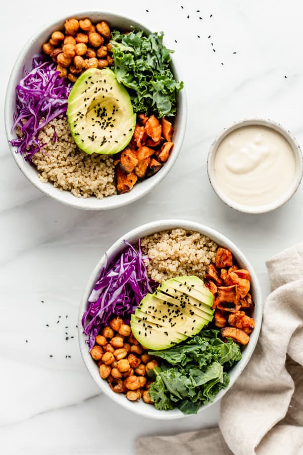 two buddha bowls with a side of tahini sauce 