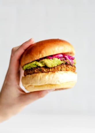 a hand holding a chickpea veggie burger filled with guacamole and picked cabbage