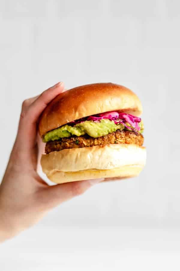 a hand holding a chickpea veggie burger filled with guacamole and picked cabbage