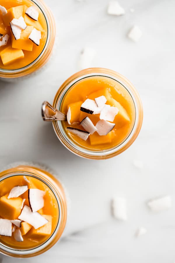 a top down image of 3 jars of coconut chia pudding with mango puree and coconut flakes