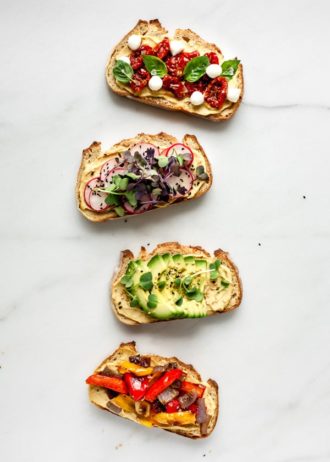 4 pieces of toast with vegetable toppings on a marble board
