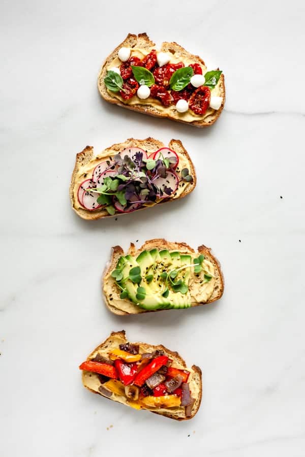 4 pieces of toast with vegetable toppings on a marble board