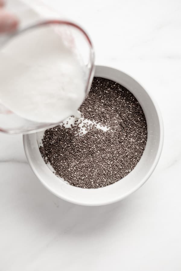 a measuring cup pouring almond milk into a bowl of chia seeds