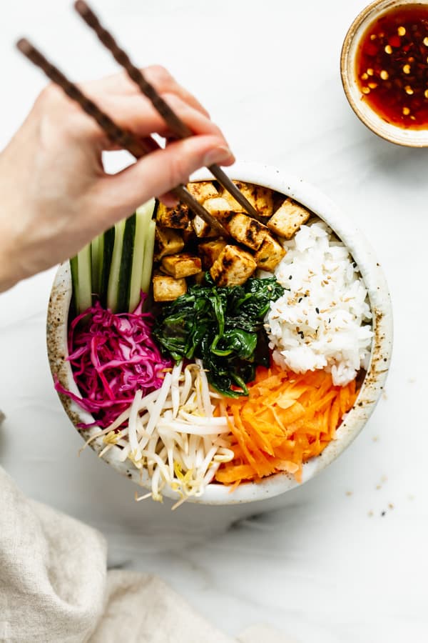 a bowl of vegan bibimbap with a hand using chopsticks