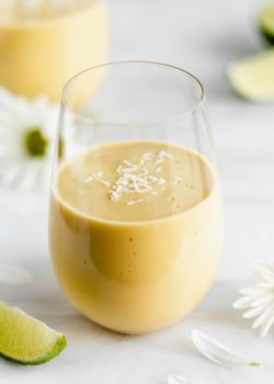 a glass of vegan mango lassi on a marble board with limes and flowers