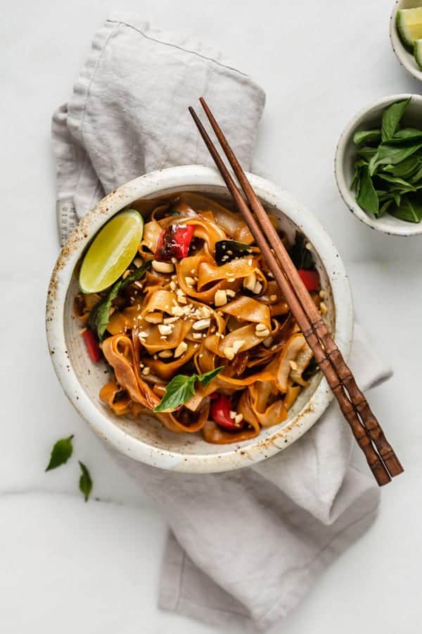 a bowl of drunken noodles on a napkin with chopsticks