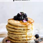 a stack of lemon poppy seed pancakes topped with blackberries and flower petals