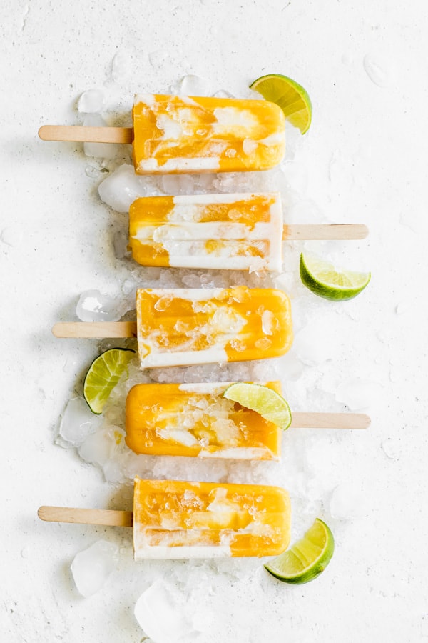 5 mango lassi popsicles on a white background with lime wedges