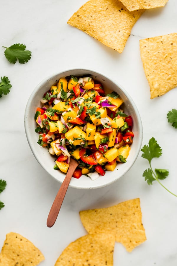 a bowl of a mango salsa with a spoon and some chips and cilantro around it