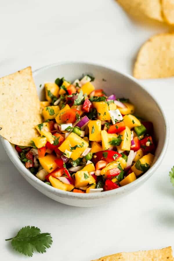 a bowl of mango salsa with a tortilla chip in it