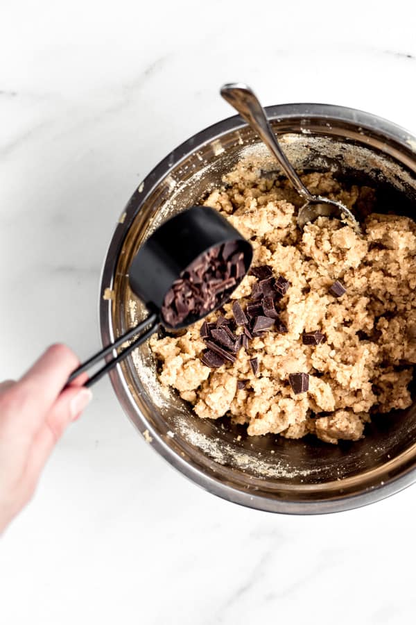 a hand pouring chocolate chunks into a bowl of blondie batter