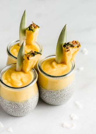 3 jars of pina colada chia pudding with pineapple wedges in them on a marble board