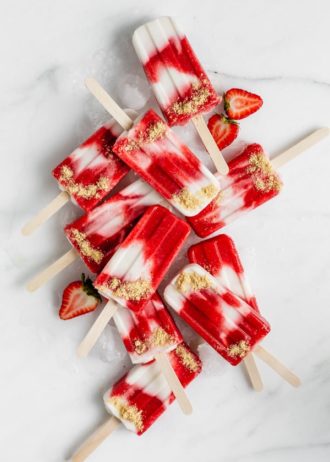 a top down view of a bunch of vegan strawberry cheesecake popsicles on a marble board