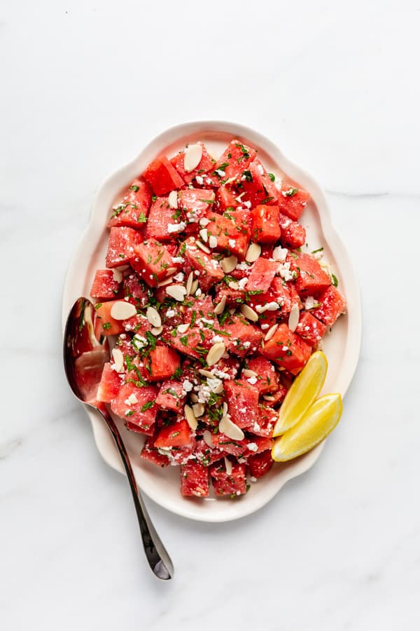 a large platter of watermelon feta salad with a serving spoon and lemon wedge