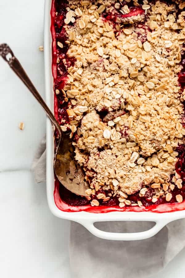 strawberry rhubarb crisp in a baking dish with a spoon in it