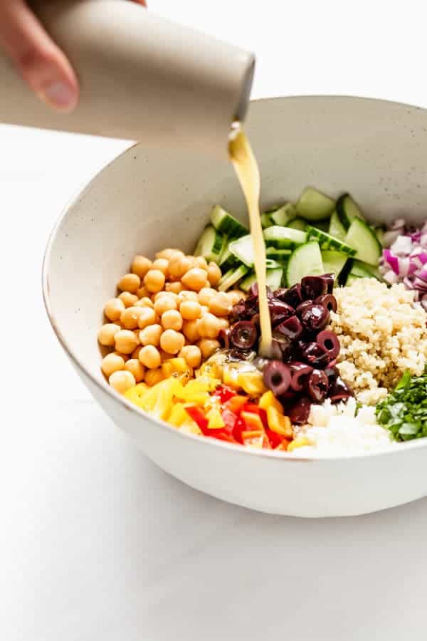 salad dressing being poured onto a quinoa salad 