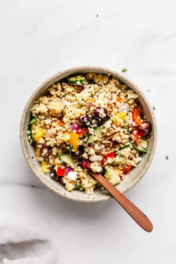 a bowl of mediterranean quinoa salad with a wood spoon