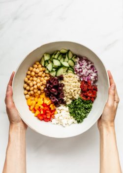 two hands holding a mixing bowl with ingredients for a quinoa salad