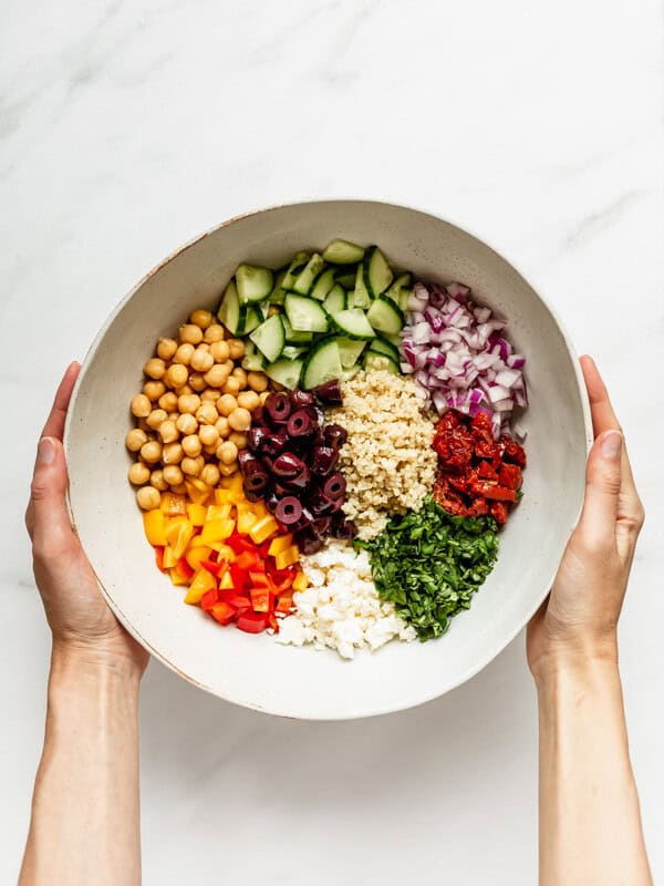 two hands holding a mixing bowl with ingredients for a quinoa salad