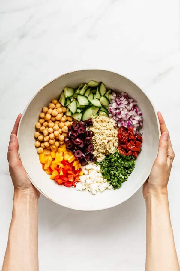 two hands holding a mixing bowl with ingredients for a quinoa salad