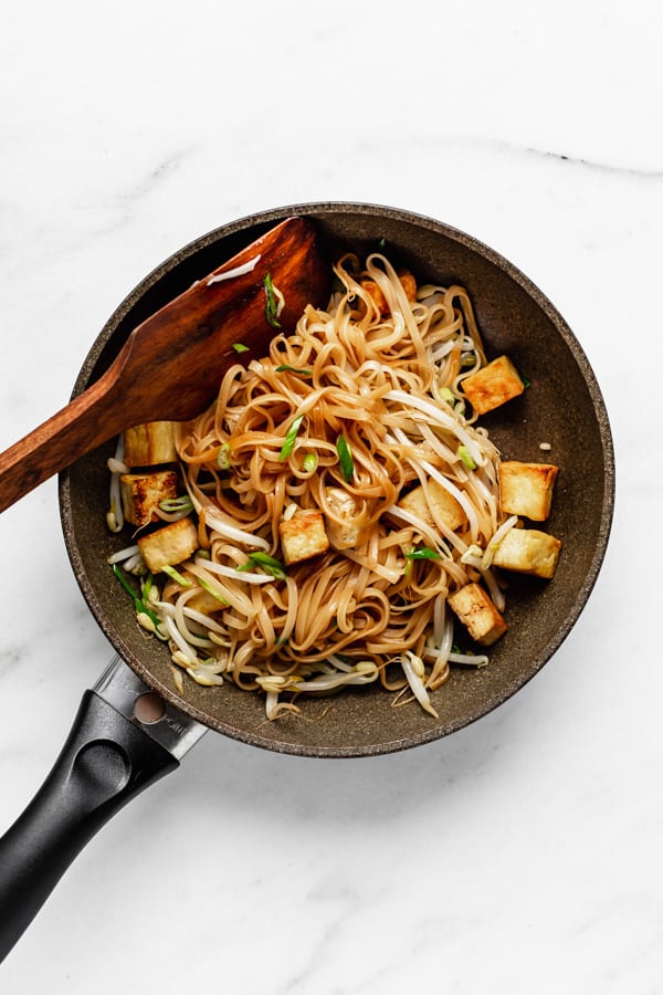 tofu, rice noodles and beansprouts in a pan with a wooden spoon