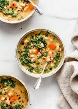 three bowls filled with white bean soup topped with chopped parsley