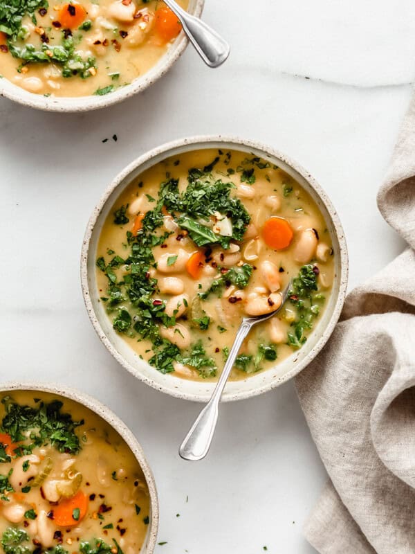 three bowls filled with white bean soup topped with chopped parsley