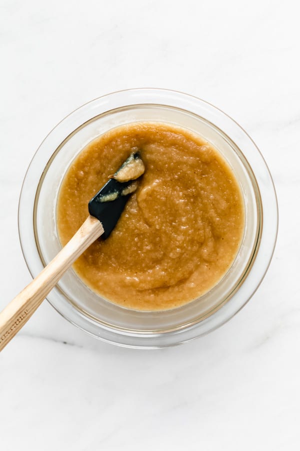 a clear mixing bowl filled with apple sauce and a spatula in it