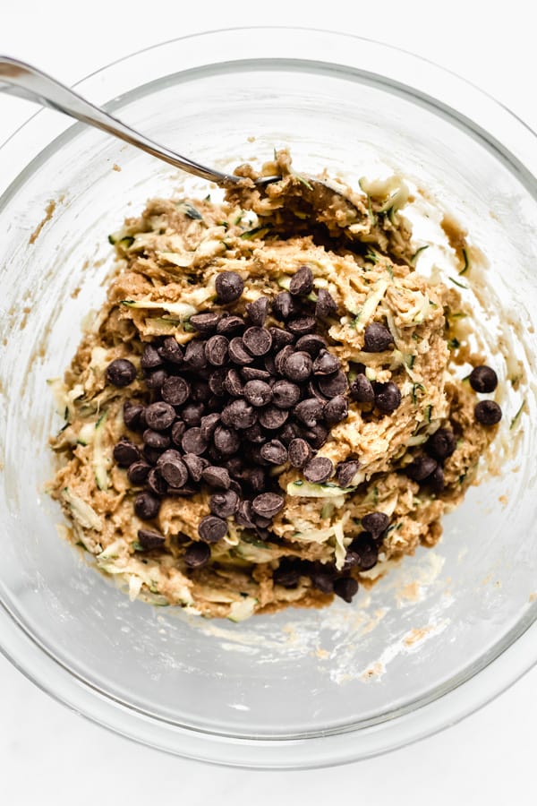 zucchini bread batter in a clear mixing bowl with a pile of chocolate chips in it