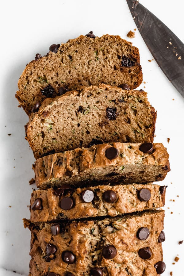 zucchini bread topped with chocolate chips sliced on a marble board