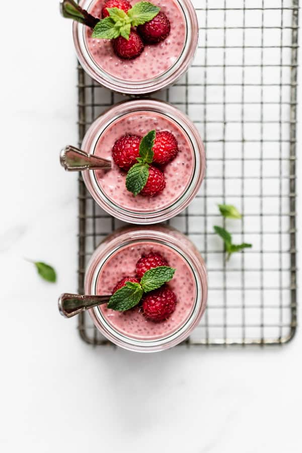 a top down image of three jars with raspberry chia pudding in them topped with fresh raspberries and a sprig of mint
