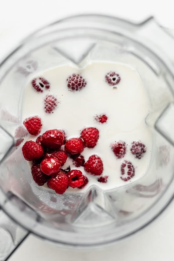 a blender with cashew milk and raspberries in it