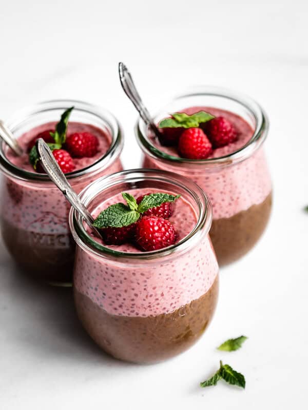 three cups of chocolate and raspberry chia pudding topped with raspberries and fresh mint